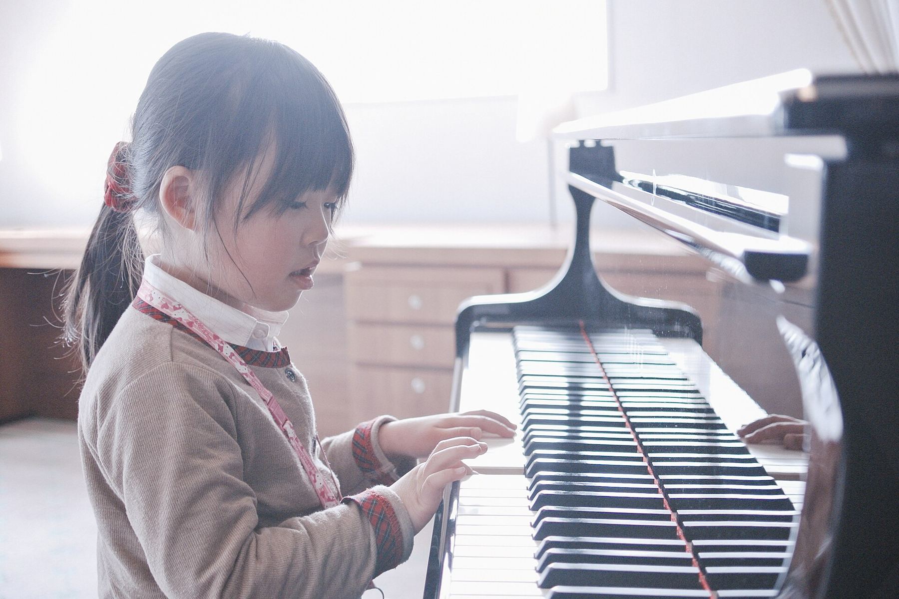 A young girl practising on a grand piano in a bright room
