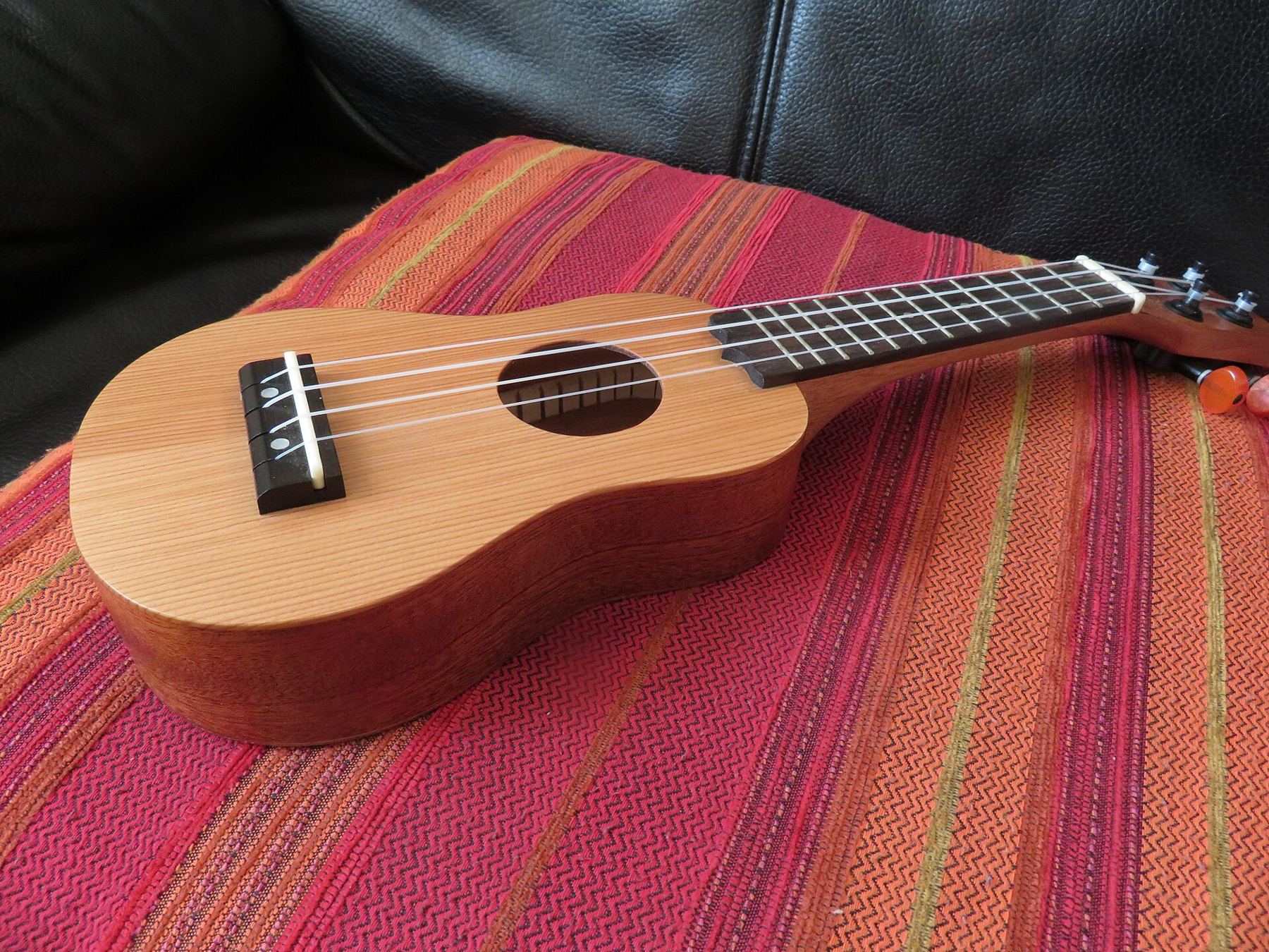 A natural wood soprano ukulele resting on a striped cushion