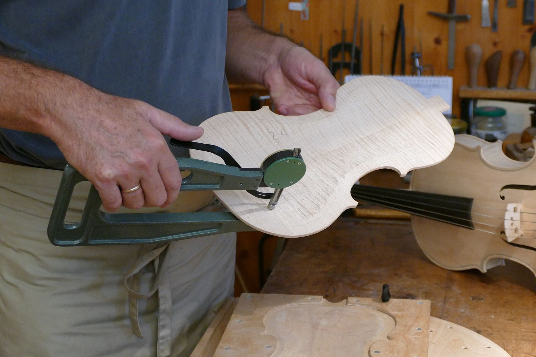 A luthier holding a carved violin plate in a clamp at the workbench