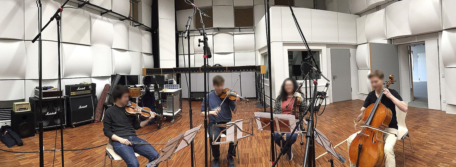 A string quartet recording in a bright, spacious live room surrounded by microphones
